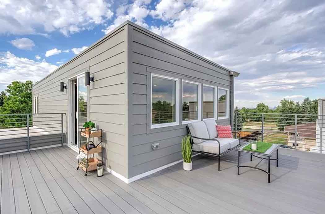 Gray rooftop deck with seating and potted plants against a blue sky.