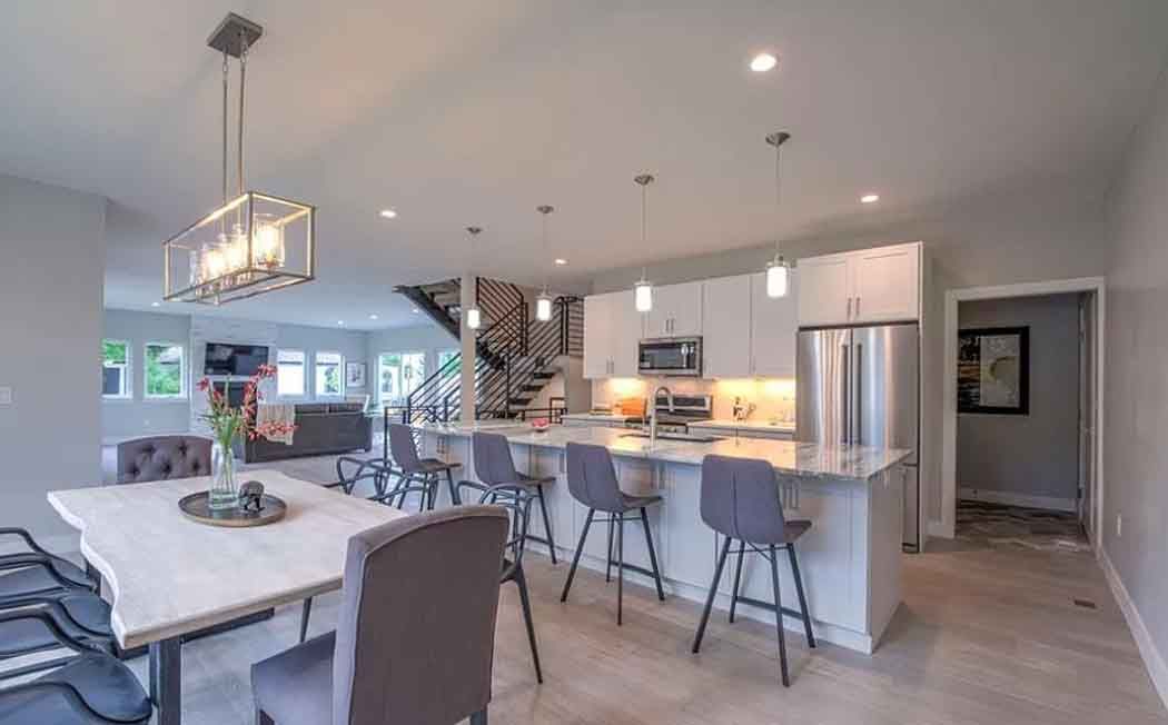 Modern kitchen and dining area with island, table, and stairs; neutral tones.