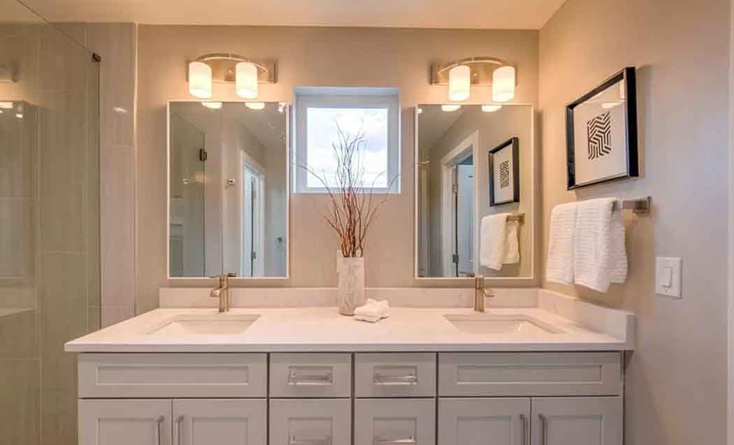 A modern bathroom with dual sinks, mirrors, and lighting. Light gray cabinets and walls.