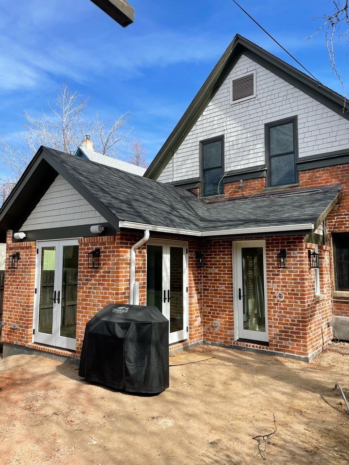 Red brick house exterior with black trim, white doors, and covered grill on a dirt patio.