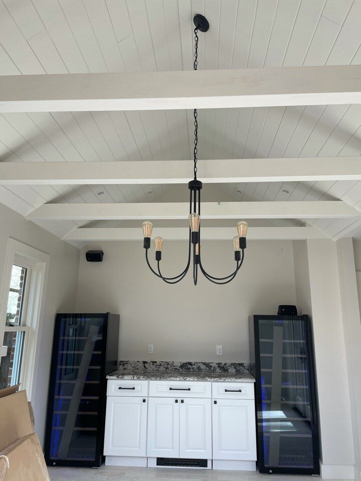 Chandelier hangs over a white cabinet bar with a granite countertop, flanked by two wine coolers.