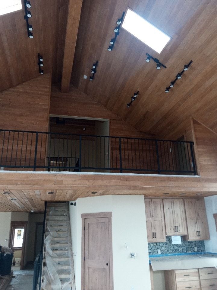 Interior of a home with a loft and wood ceiling, track lighting, and a staircase.