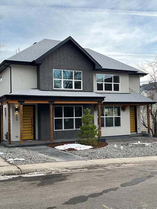 Two-story duplex with grey brick accent, cream siding, and yellow doors. Snow on the ground.
