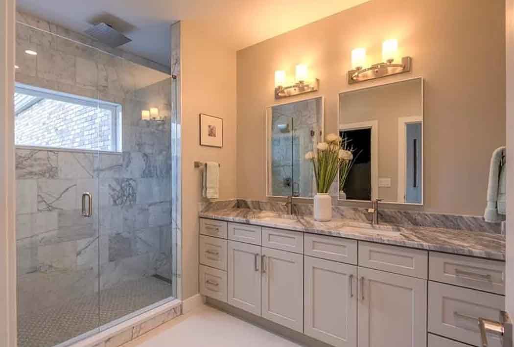 Bathroom with a marble-tiled shower, a white vanity with two sinks, and wall-mounted lighting.