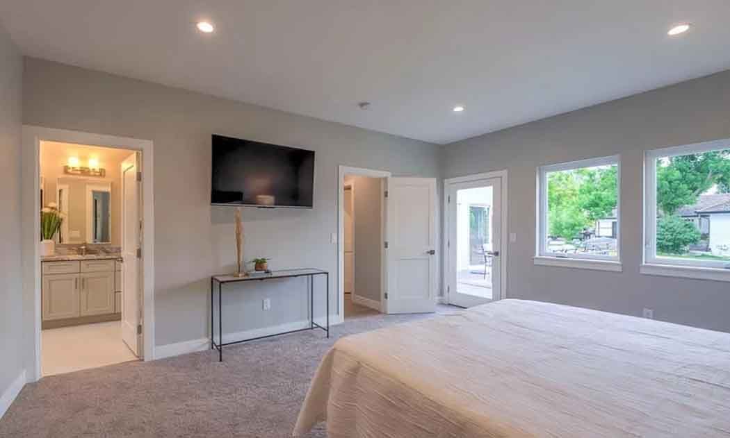 Bedroom with a large bed, TV on wall, doors, windows, and a view of the outside.