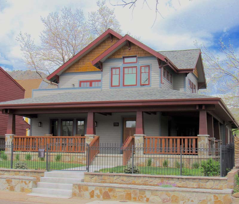Craftsman-style house with gray siding, brown trim, and a front porch behind a low stone wall and fence.
