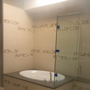 Bathroom with oval tub, glass shower door, and decorative tile.