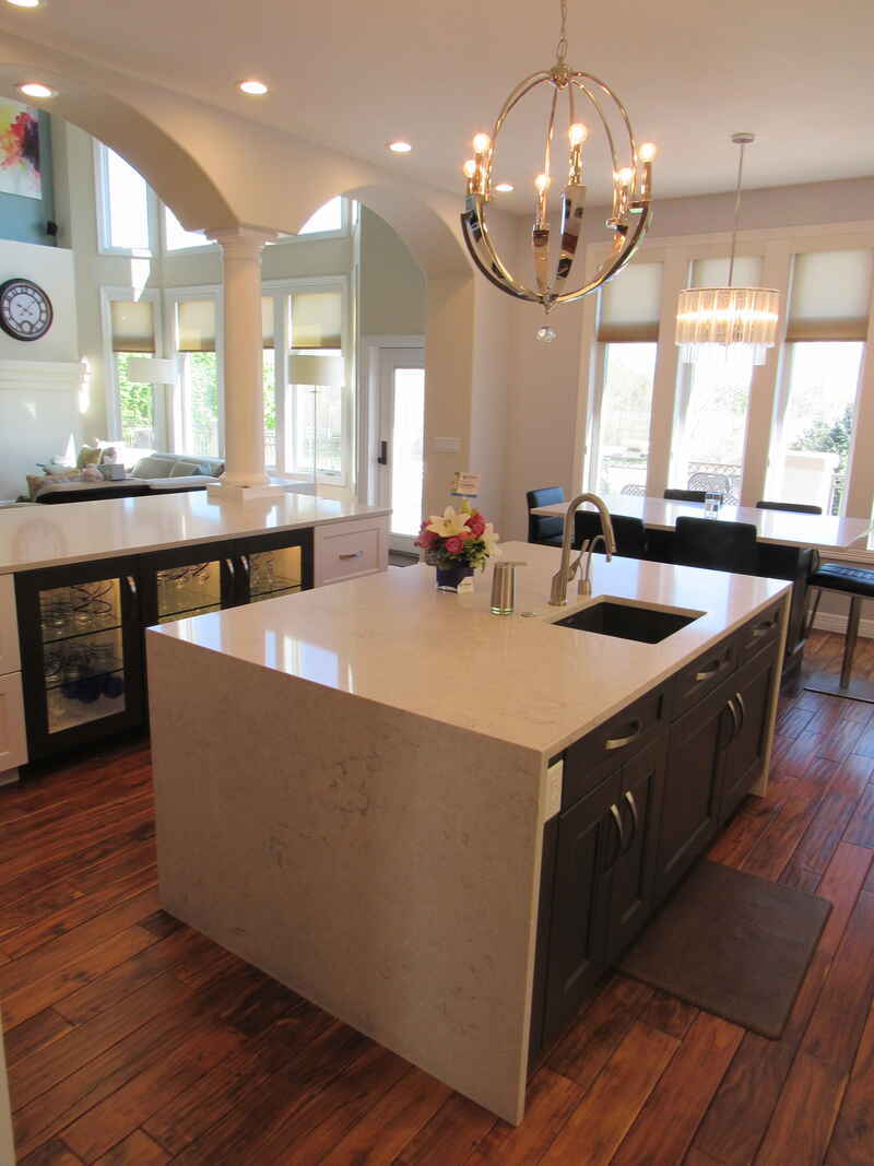 Kitchen with a white countertop island and dark cabinets; dining area in the background.