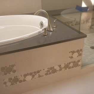 Bathroom with a white bathtub, gray countertop, and patterned tile detail.
