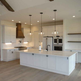 White kitchen with island, pendant lights, and stainless steel appliances.
