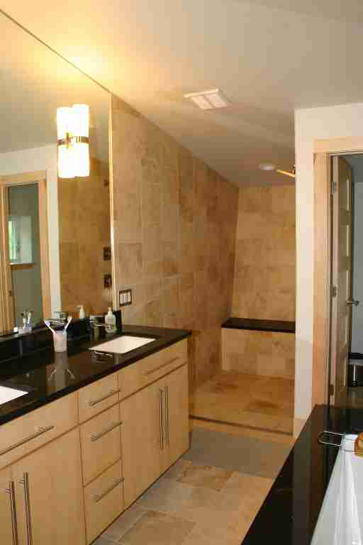 Modern bathroom with light wood vanity, black countertop, stone shower, and recessed lighting.