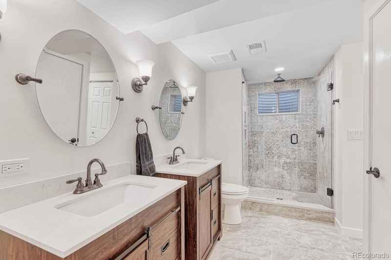 Bathroom with two sinks, a shower, and a toilet. Brown vanities, white countertops, and a gray tiled shower.