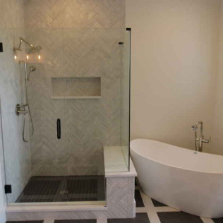 Modern bathroom with glass shower, white bathtub, and patterned tile floor.