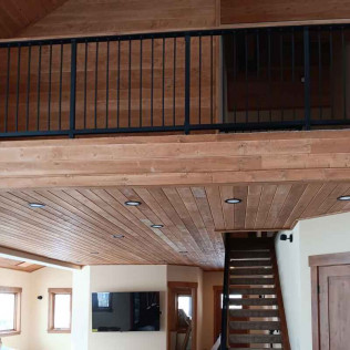 Wooden-paneled ceiling and loft with black railing. Staircase leads up to the loft.