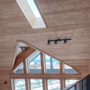 Wooden ceiling with a skylight and triangular window; snow visible outside.