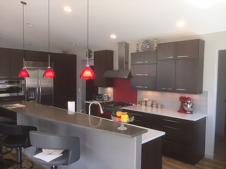 Modern kitchen with dark cabinets, red backsplash, stainless steel appliances, and red pendant lights.