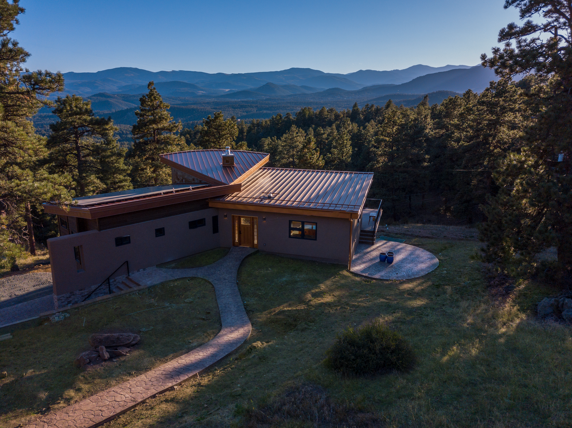 House with a metal roof and adobe-style exterior set on a hillside with a mountainous backdrop.