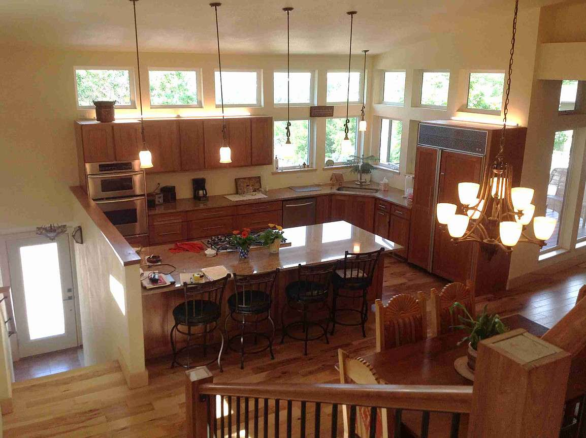 Spacious kitchen with island, wooden cabinets, large windows, dining table, and staircase.