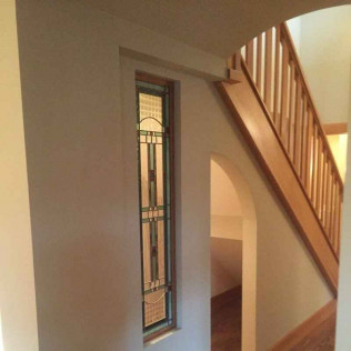 Staircase with wood banister and narrow stained glass window in a neutral-toned hallway.