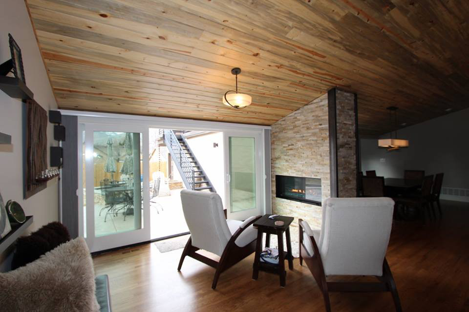 Modern living room with wood ceiling, fireplace, and two white armchairs facing sliding glass doors.