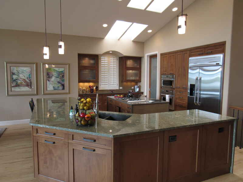Spacious kitchen with a large island, two paintings, and a skylight. Brown cabinets and granite countertops.