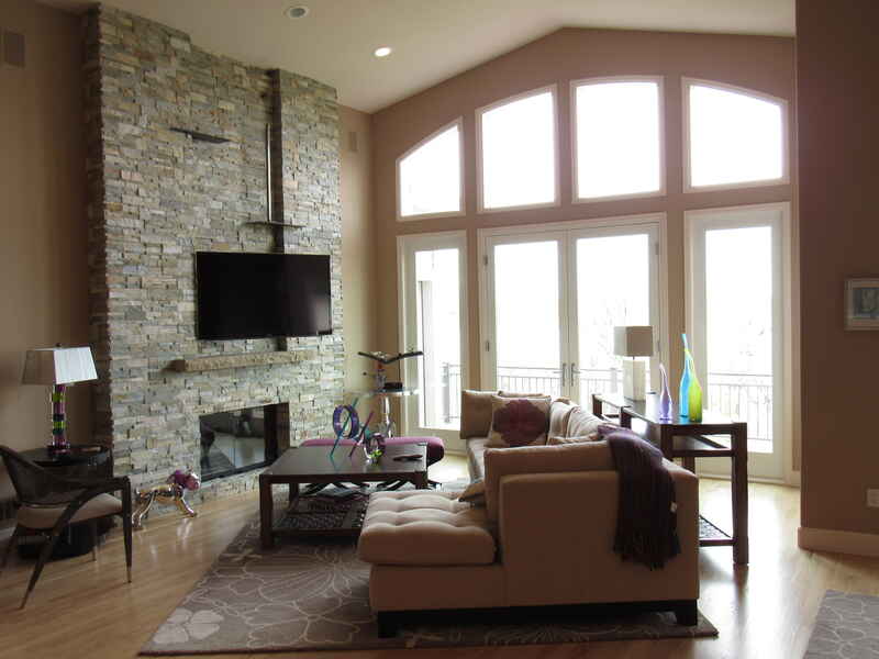 Living room with stone fireplace, large windows, and tan sofa.