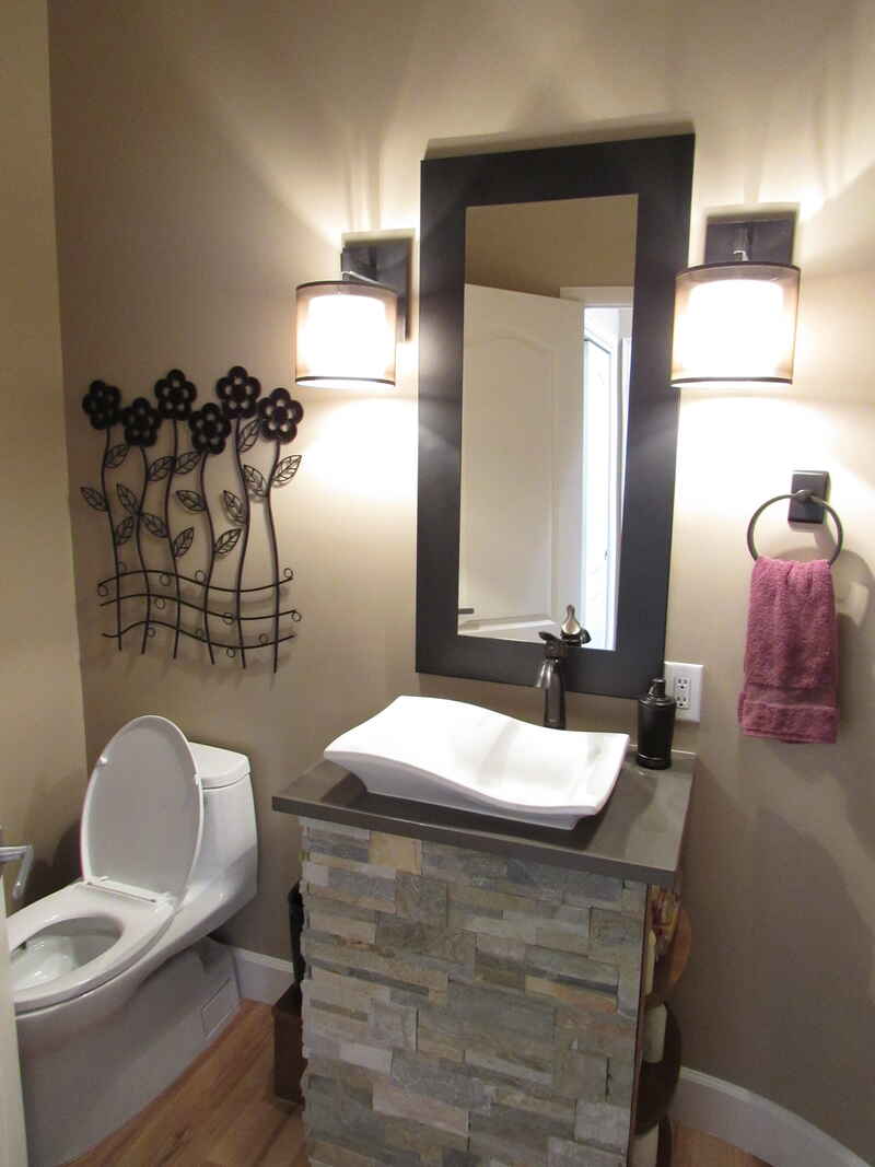 Bathroom with stone-covered vanity, vessel sink, dark framed mirror, and sconce lighting. A toilet and a towel rack are also visible.