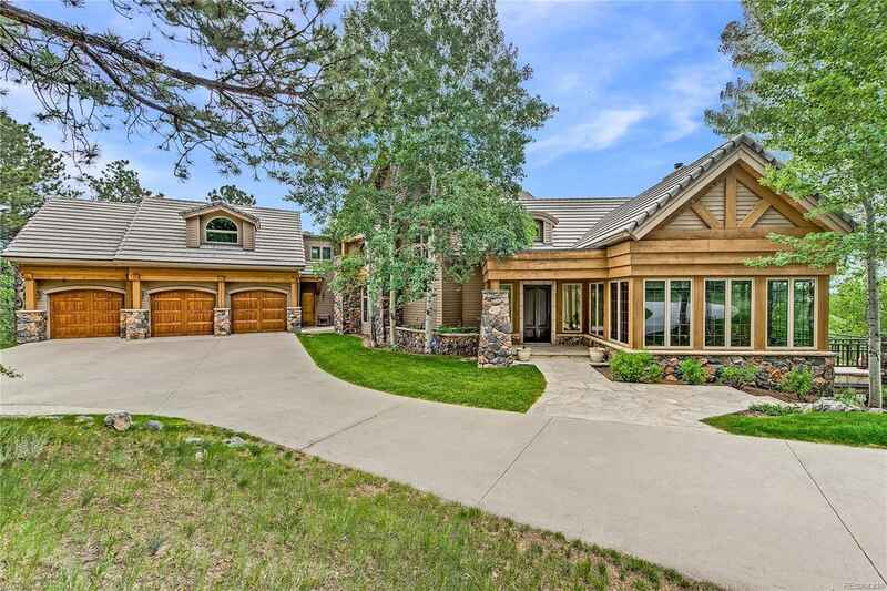 A large, wood-paneled house with a stone facade and a three-car garage, set amidst trees.