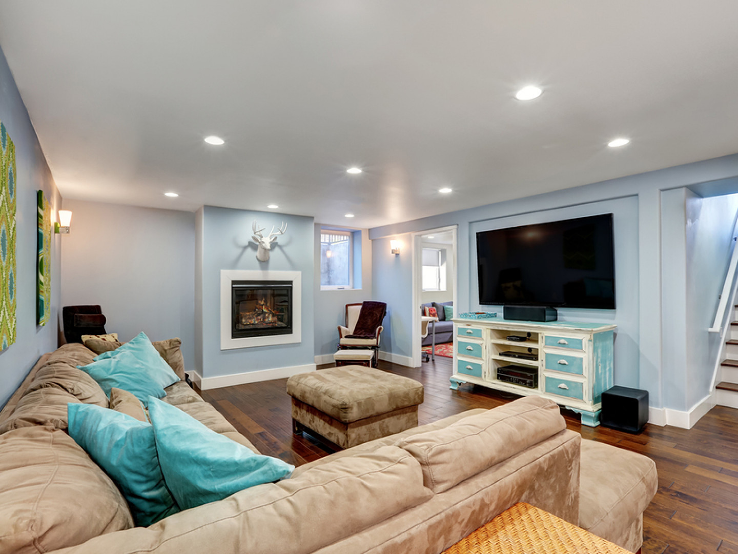 Cozy basement living room with fireplace, TV, sectional sofa, teal accents, and stairs.