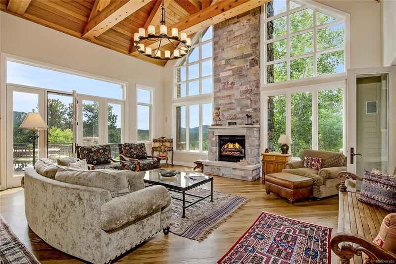 Spacious living room with fireplace, high windows, and mountain view. Light wood ceiling, tan sofa, and rug.