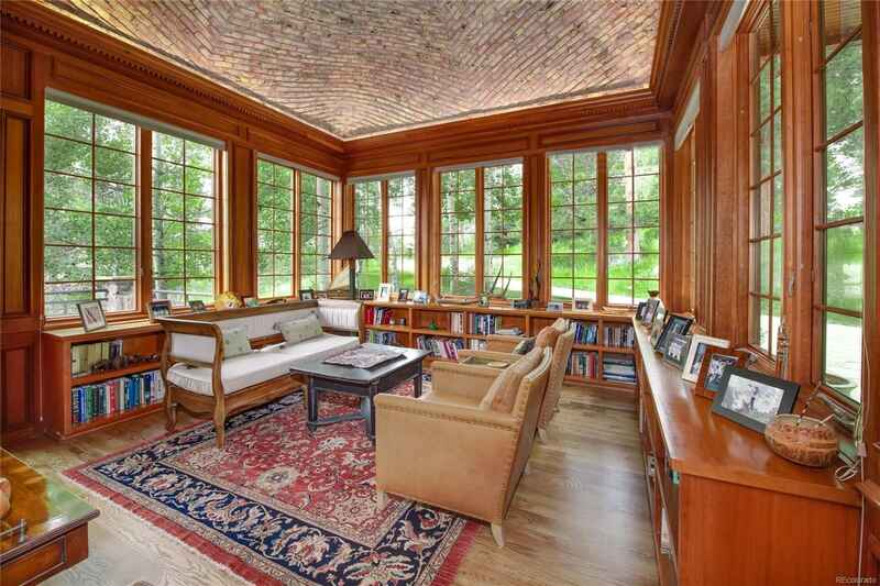 Sunroom with wood paneling, windows, and a patterned rug. Furnished with seating and bookshelves.