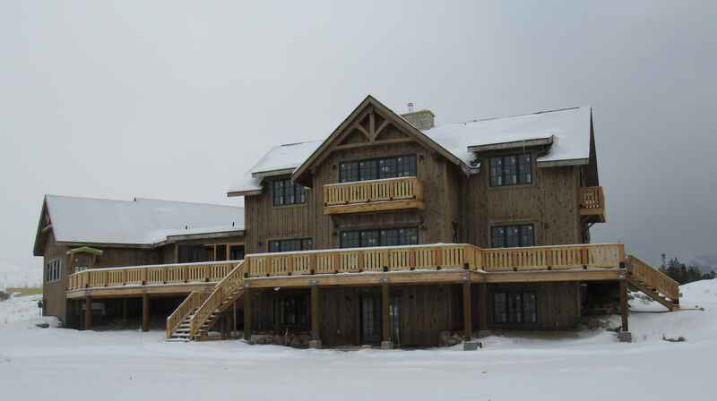 Large, brown wood house with snow-covered roof and deck, set against a cloudy sky.