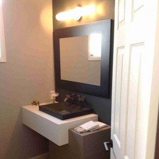Modern powder room with a black sink, floating white vanity, and large dark-framed mirror.