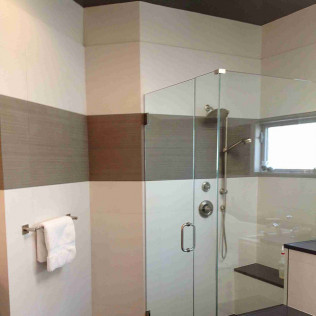 Bathroom with a glass shower, white and brown tile walls, a towel rack, and a small window.