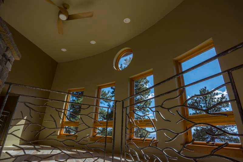 Interior view of a second-story landing with windows, metal railing, and a ceiling fan.