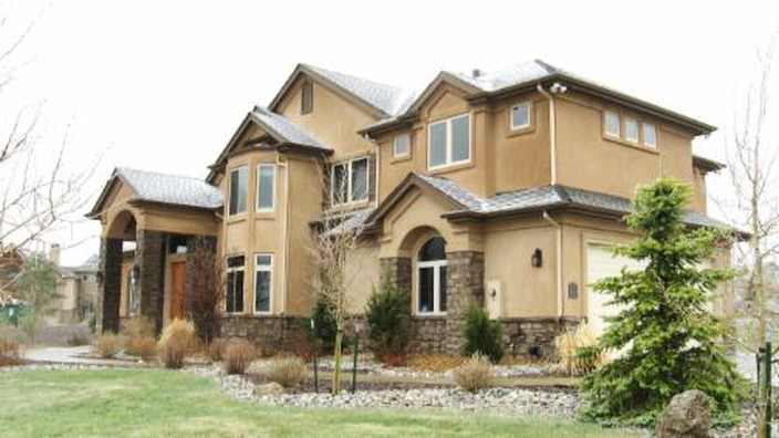 Two-story beige house with stone accents, arched windows, and a green lawn.