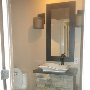 Bathroom with toilet, sink, mirror, and sconce lights. Beige walls, stone vanity, and dark-framed mirror.