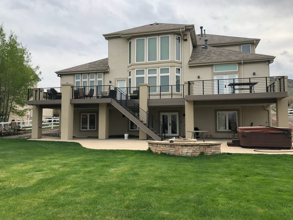 Two-story beige house with decks, a hot tub, and a lawn, under a cloudy sky.