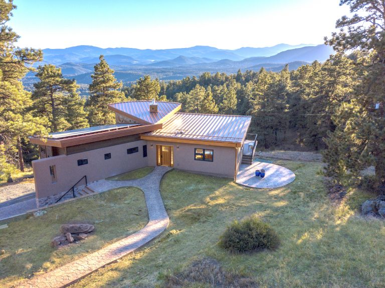 Modern home with a silver roof, overlooking a mountainous landscape and a circular patio.