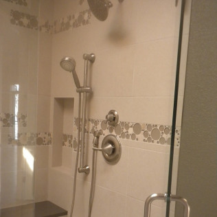 Shower with white tiles, silver fixtures, and a glass door. Includes handheld shower head and wall niche.
