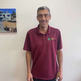Man in burgundy polo shirt smiles, stands near a painting on a white wall.