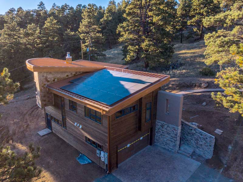 Modern wooden house with solar panels on roof in a wooded area.