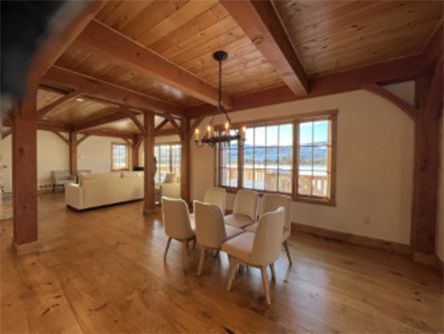 Dining room with wooden beams, table, chairs, and windows with outdoor view.