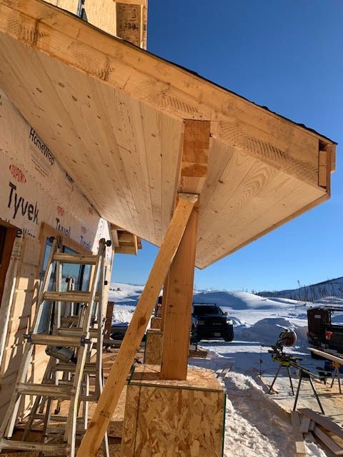 Wooden porch under construction; boards, support beams, ladder, snowy landscape in background.