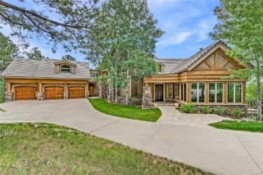 Rustic home with a garage, driveway, and surrounding trees under a blue sky.