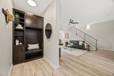 Entryway with dark wood built-in storage, leading to a living room with stairs, black sofa, and wooden floors.