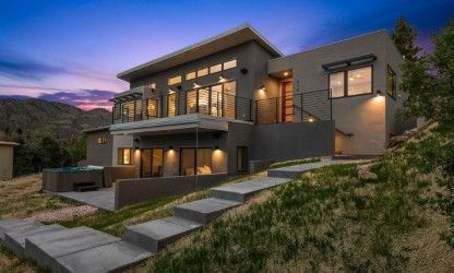 Modern two-story house with large windows, patio, and steps leading up from the grassy yard.