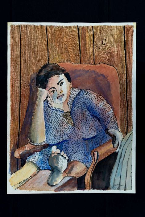 Woman in blue top, seated, resting head on hand, foot up on armrest. Brown chair, wood-paneled wall.