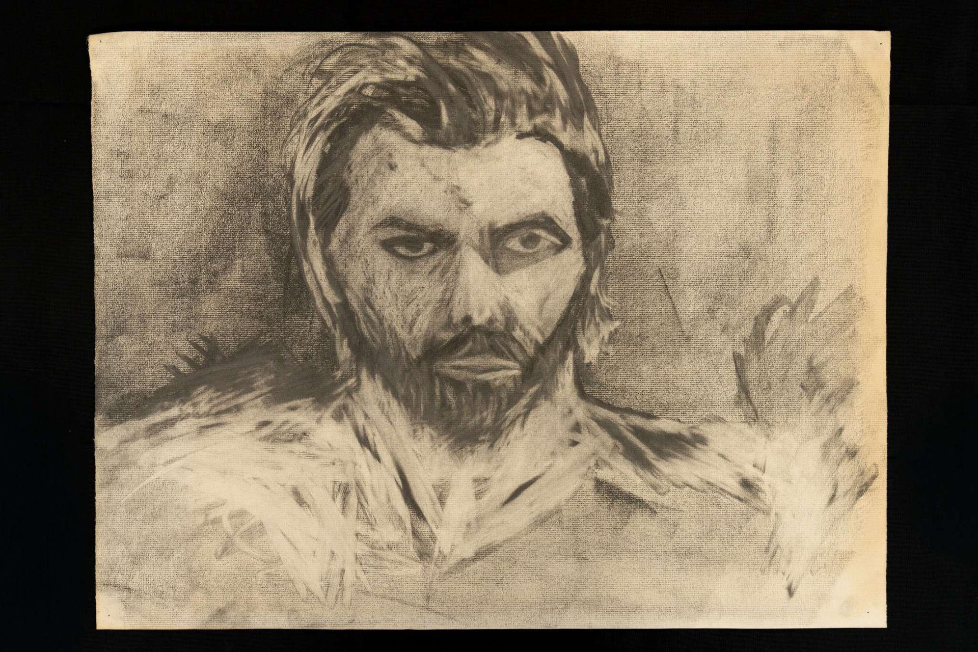 Charcoal portrait of a man with a beard, intense gaze, and a slight smirk.