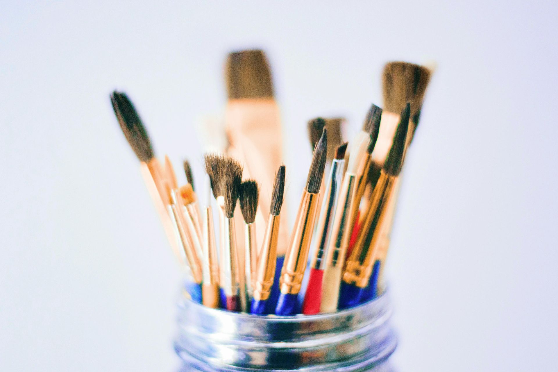 Paintbrushes in a glass jar, various sizes, bristles up, gold handles, blue rim.